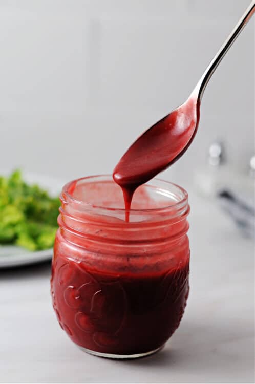 raspberry balsamic vinaigrette dressing pouring from a spoon into a jar