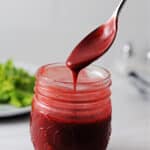 spoon pouring raspberry balsamic vinaigrette dressing over a small jar