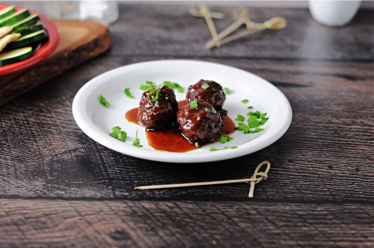 3 grape jelly bbq meatballs on a small white plate with sauce pooling around them