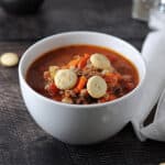 white bowl of hamburger barley soup, 3 oyster crackers on top