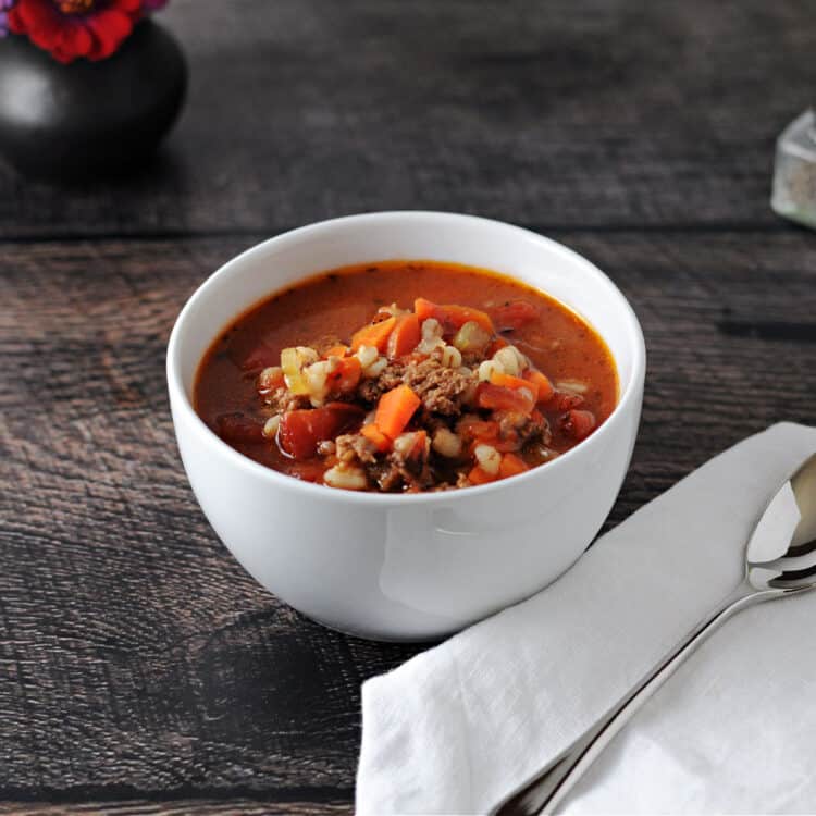 white bowl of barley soup with a napkin and spoon next to it