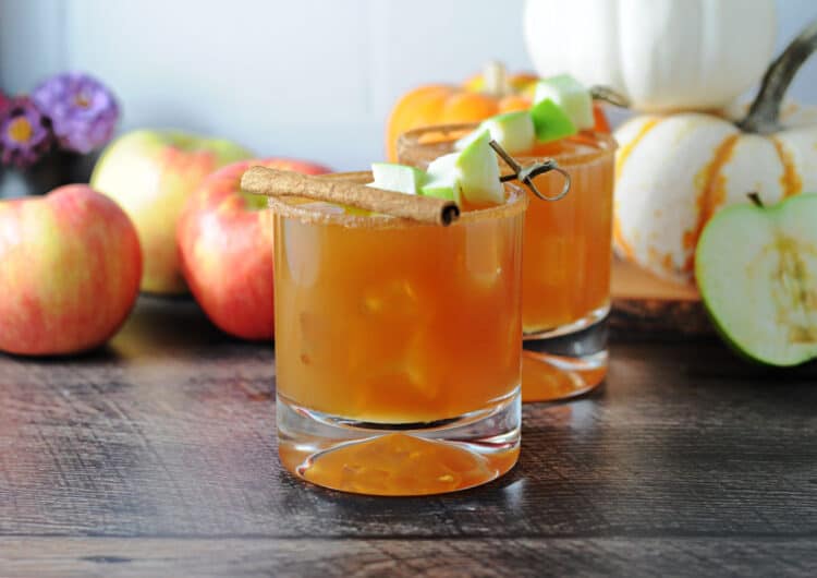 2 caramel apple cider cocktails with whole apples and small pumpkins behind