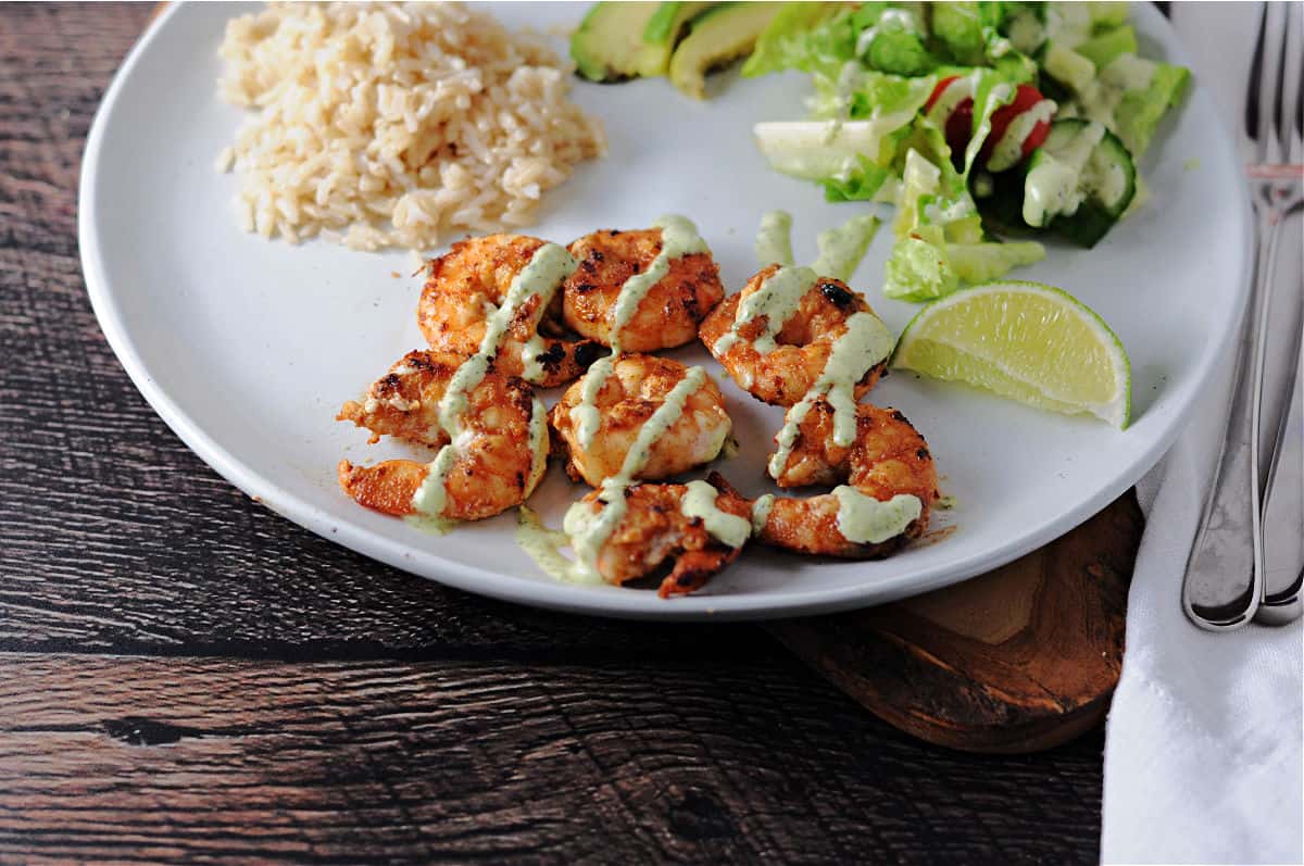 Chili lime shrimp on a plate with salad and rice, drizzled with cilantro lime sauce