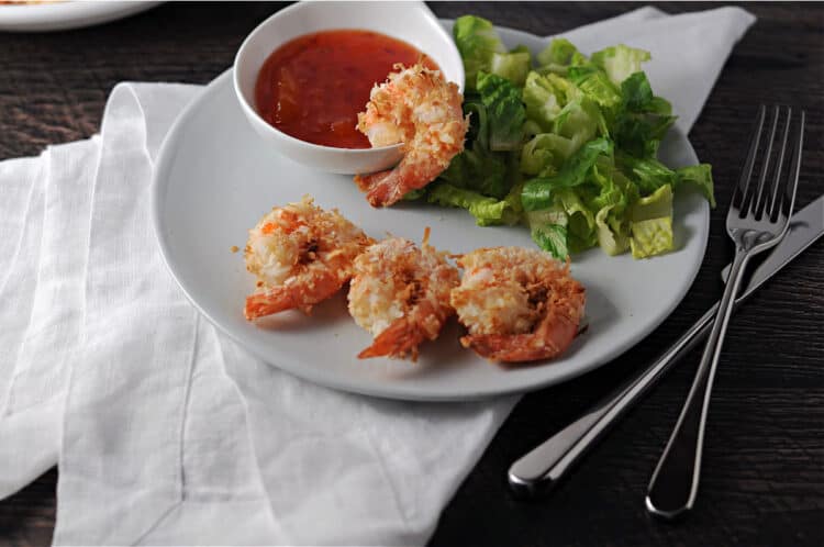 air fried coconut shrimp on a small plate with dipping sauce and a green salad