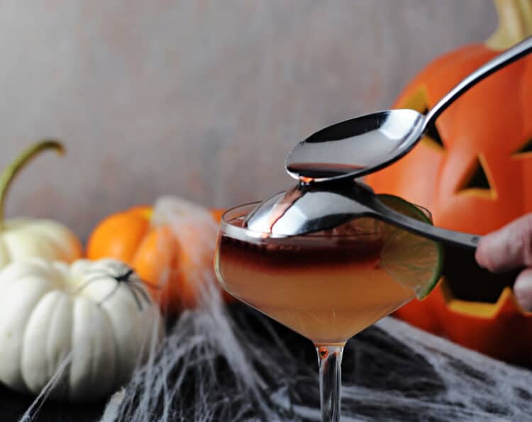 pouring wine over an inverted spoon to create a layer on top of the drink