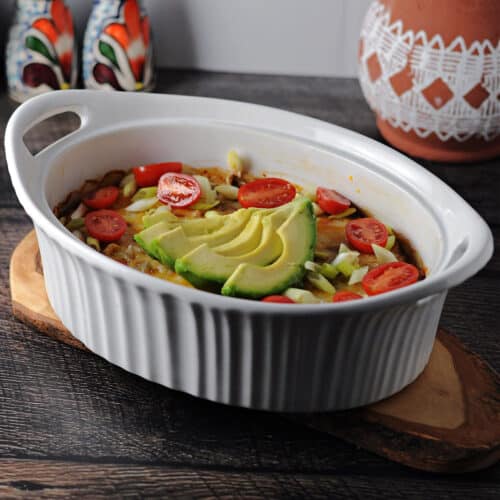 keto taco casserole in an oval dish garnished with green onions, tomatoes and a sliced avocado