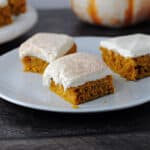 3 pumpkin bars with cream cheese frosting on a white plate