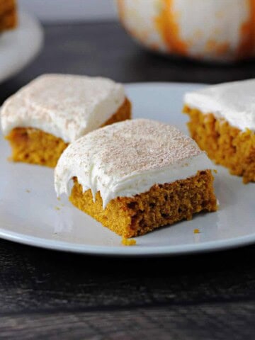 3 pumpkin bars with cream cheese frosting on a white plate