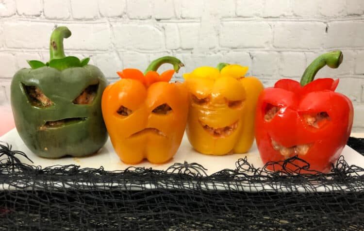 4 stuffed peppers with carved faces, all lined up