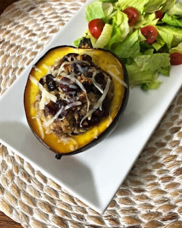 stuffed acorn squash on a white rectangular platter with a green salad