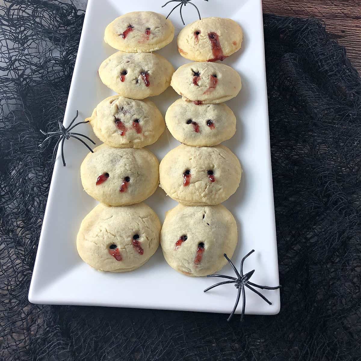 Vampire kiss cookies on a rectangular white plate, a couple spiders lurking around
