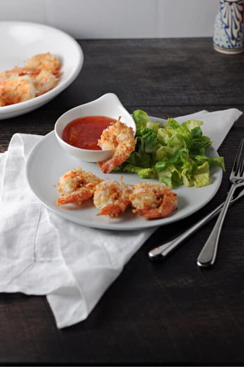 air fryer coconut shrimp on a small plate with dipping sauce and a green salad