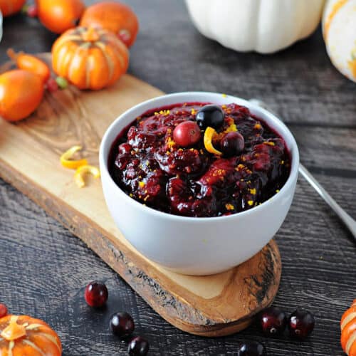 a bowl of sugar free keto cranberry sauce surrounded by decorations with a spoon nearby