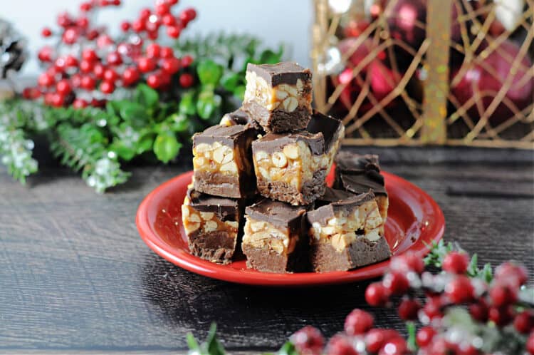 Stacked pieces of snickers fudge on a red plate surrounded by holiday decor