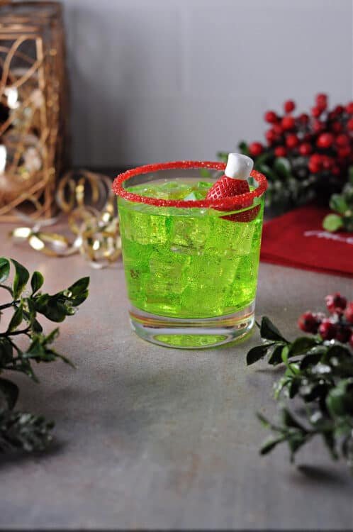 grinch cocktail on the rocks, garnished with a strawberry and rimmed with red sugar