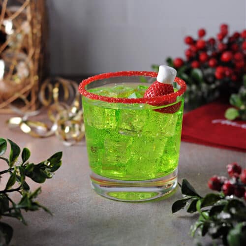 grinch cocktail on the rocks in a glass rimmed with red sugar