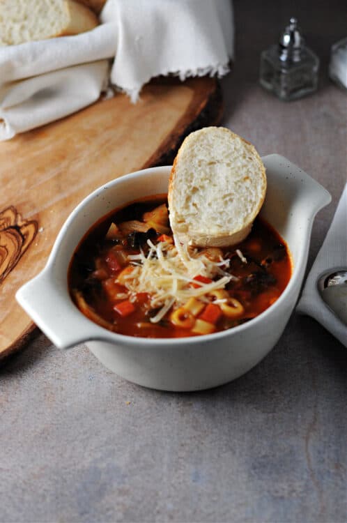 cup of instant pot minestrone soup garnished with shredded parmesan cheese and a slice of bread