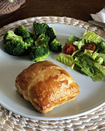 chicken in puff pastry hand pie on a plate with salad and broccoli
