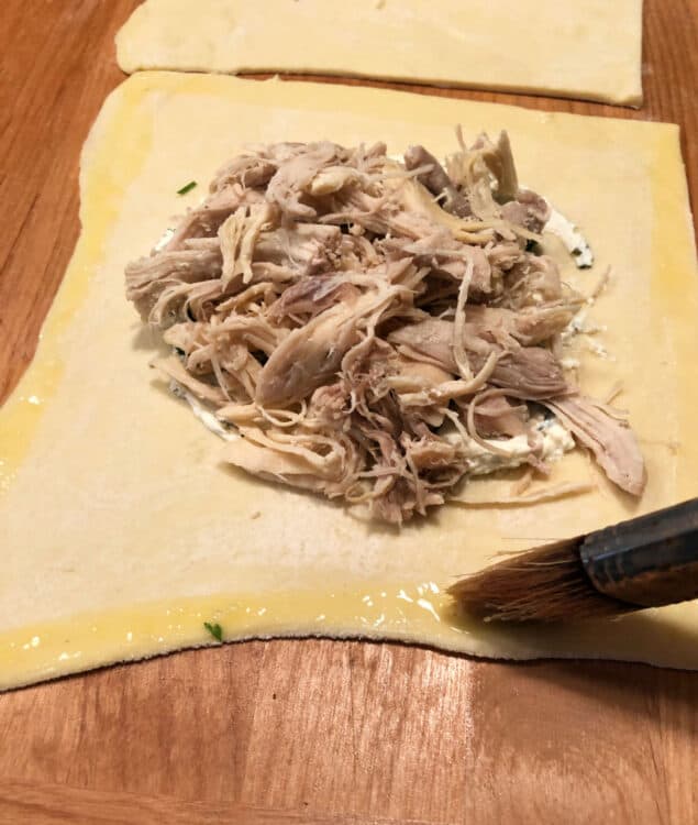 brush applying egg wash to edges of pastry which has shredded meat in the middle