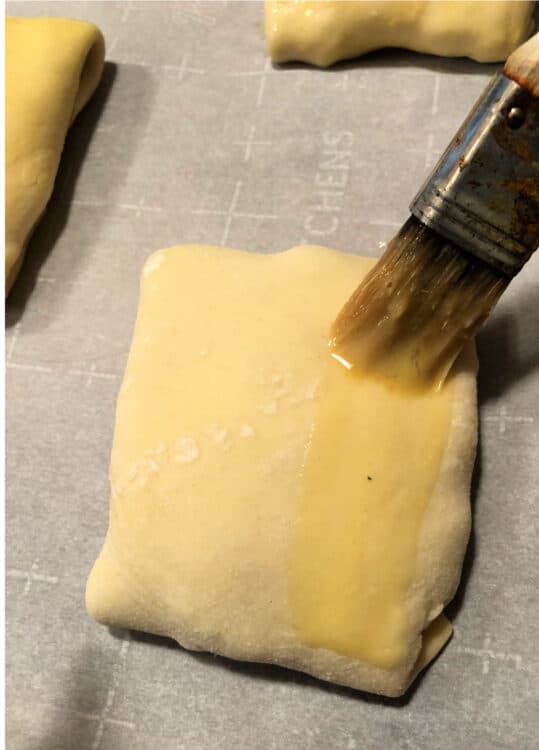 pastry on a baking sheet being brushed with egg wash