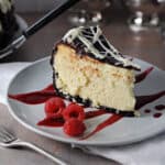slice of white chocolate cheesecake with oreo crust, topped with ganache, on a small plate with raspberries