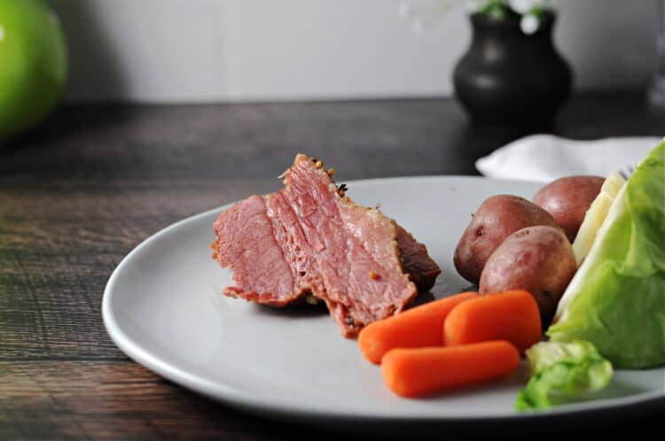 instant pot cooked corned beef on a palte with cabbage, carrots, and potatoes.