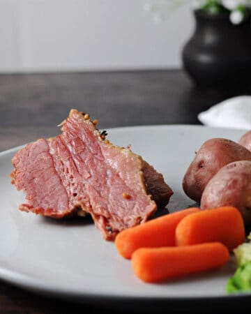 sliced instant pot corned beef on a plate with cabbage, carrots, and potatoes.