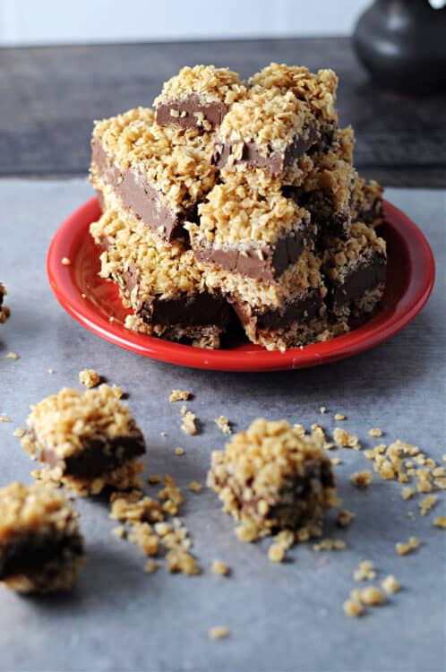 pile of chocolate peanut butter oatmeal bars on a small red plate with a few small bars and oatmeal in front of it.