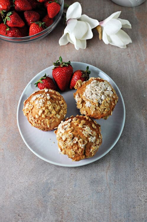 3 starwberry greek yogurt muffins on a plate with 3 fresh strawberries.