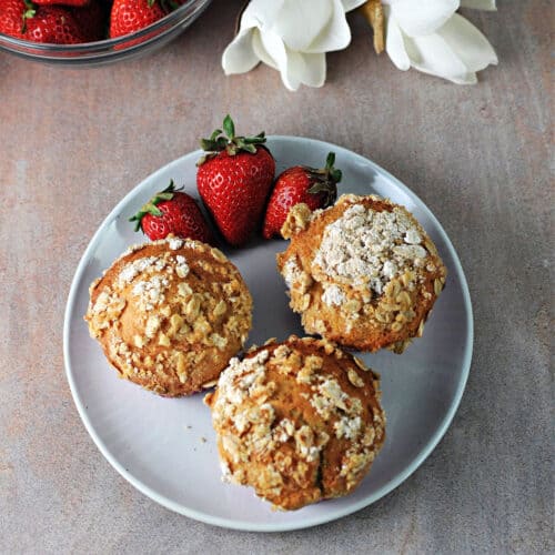 3 strawberry greek yogurt muffins on a plate with fresh strawberries.