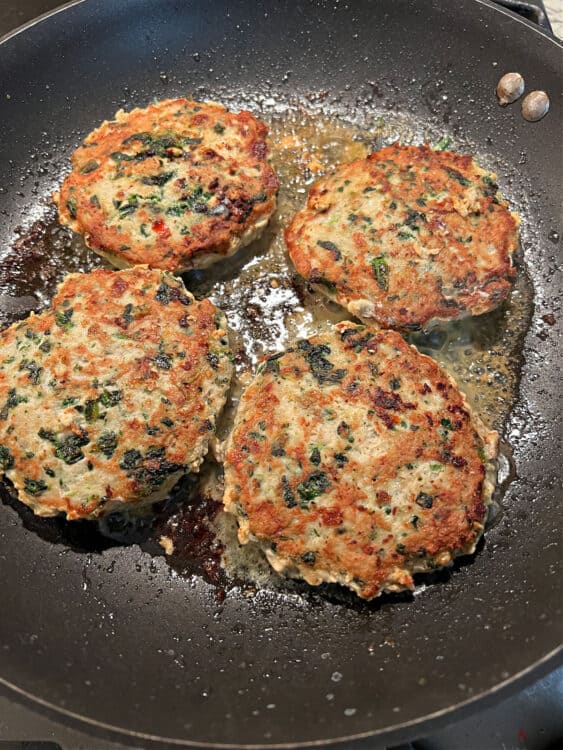 chicken feta spinach burgers cooking in a pan.