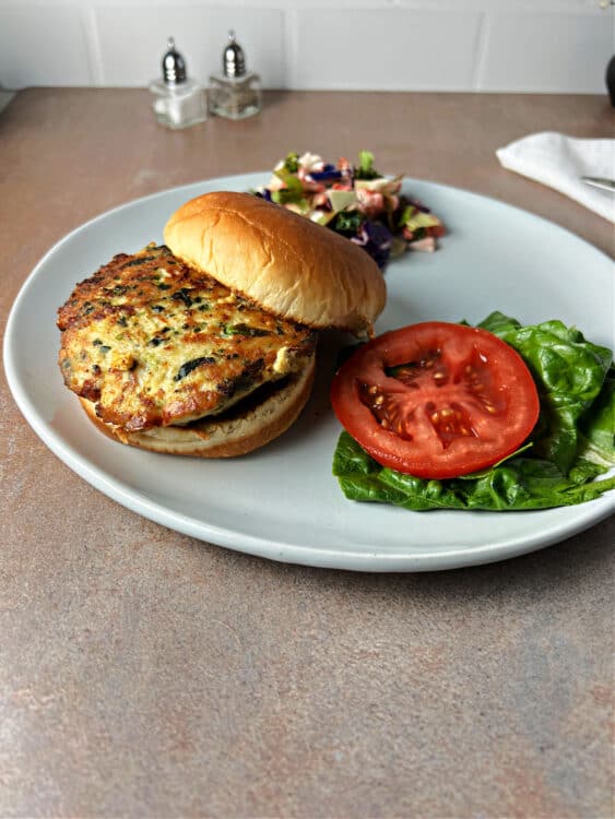 chicken feat spinach burger on  bun served on a plate.