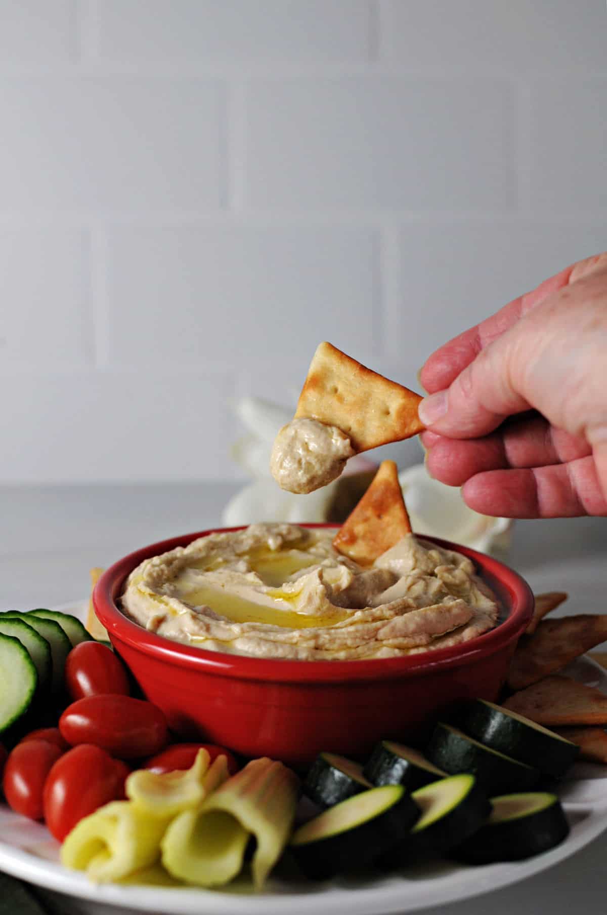 hand holding a cracker dipping into a bowl of hummus.