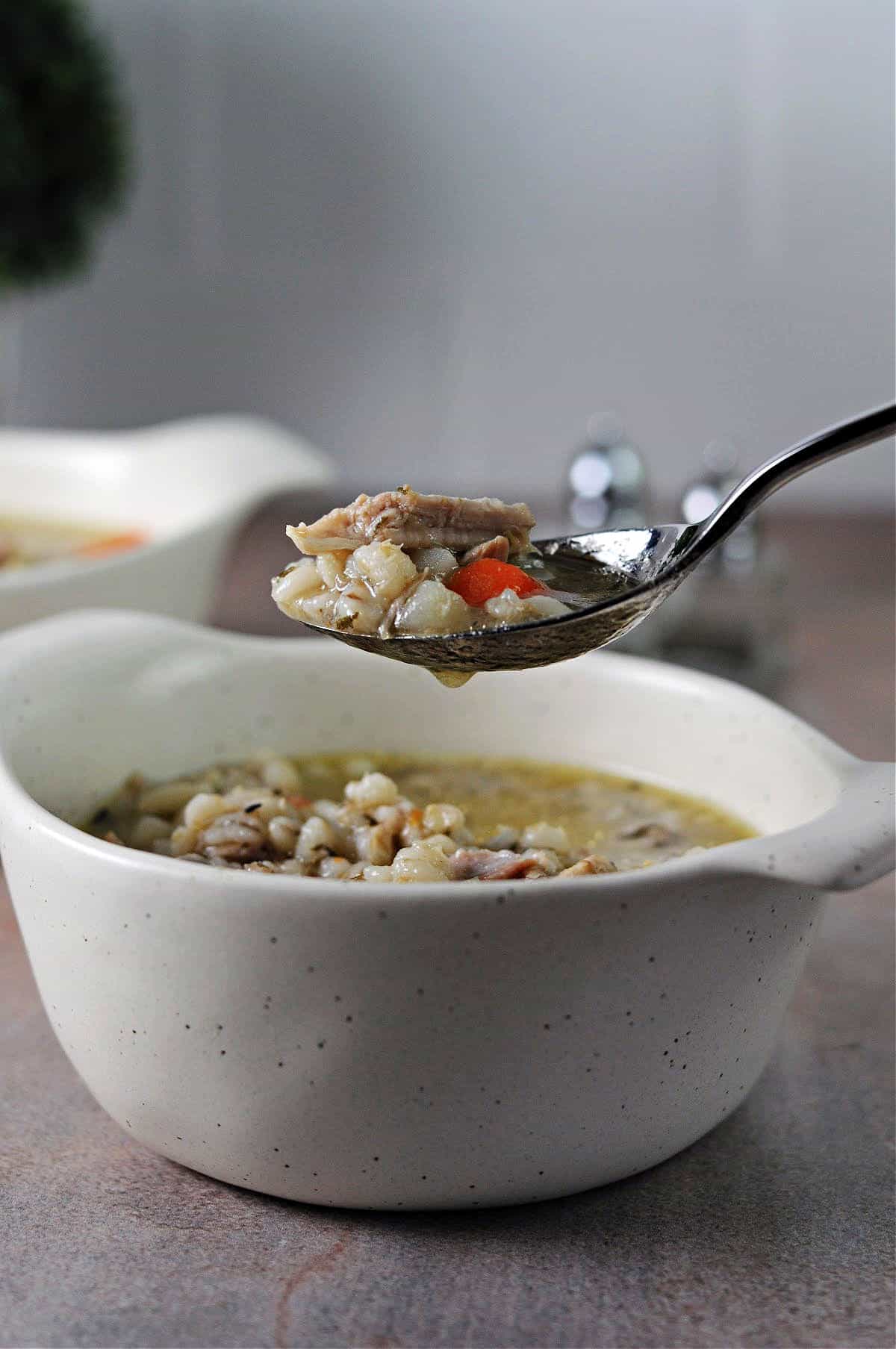 spoon of chicken barley soup over a bowl of the soup.