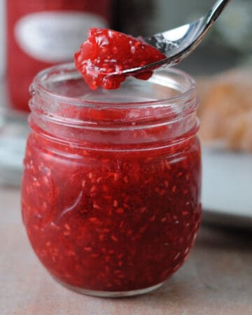 jar of raspberry freezer jam with a spoon holding some above it.