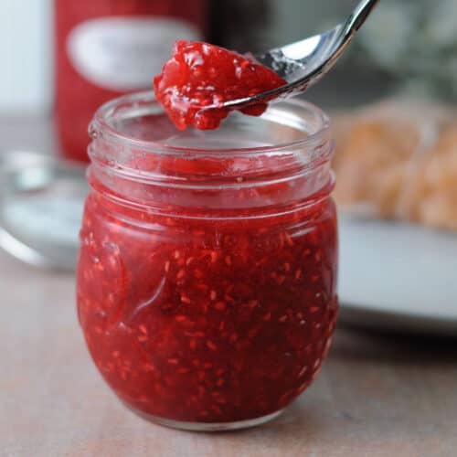 jar of raspberry freezer jam with a spoon holding some above it.