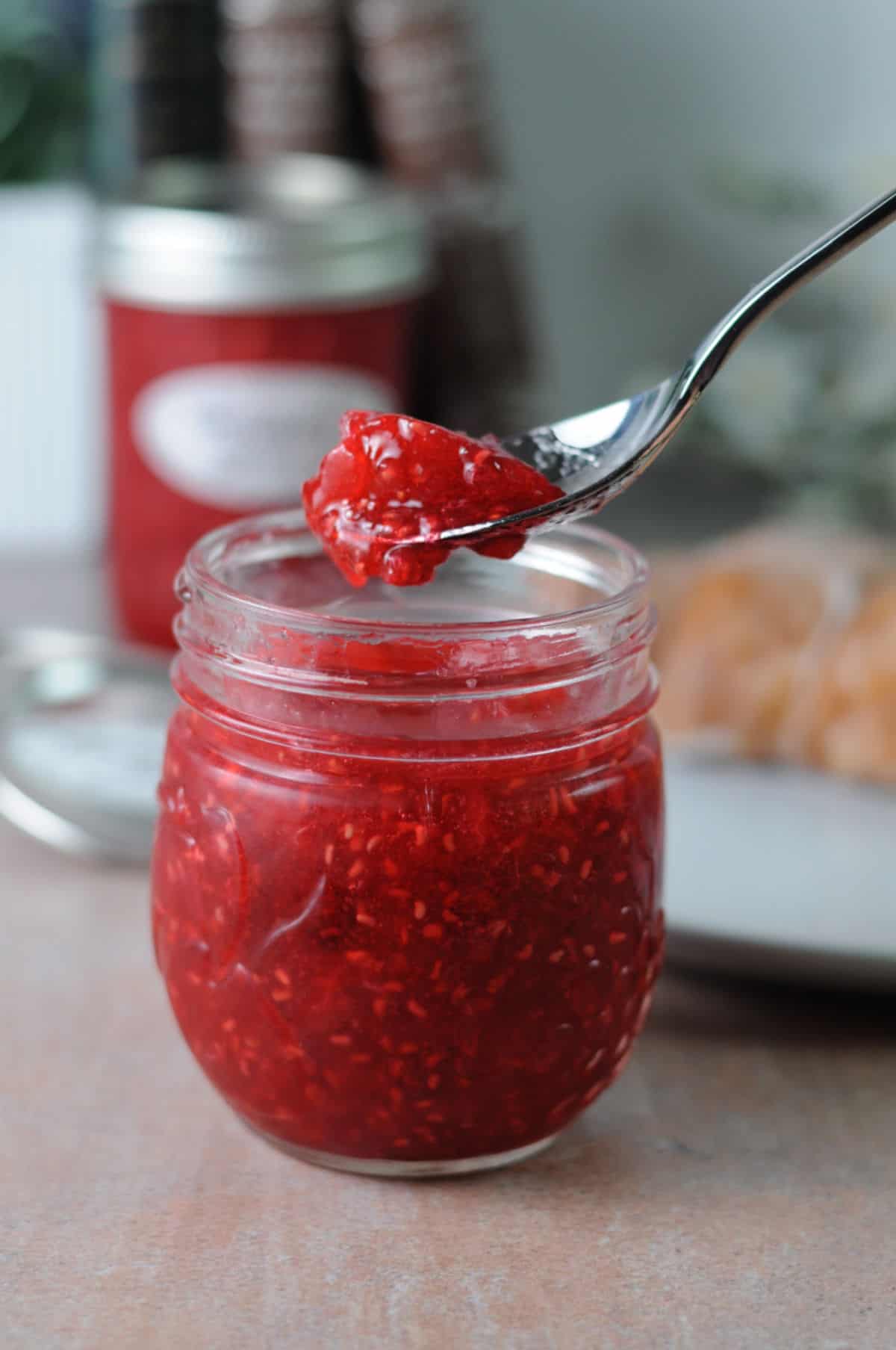 spoon of raspberry freezer jam held above a full jar of jam.