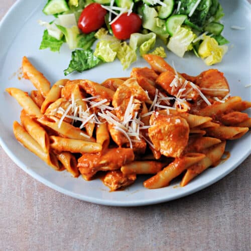 penne alla vodka sauce with chicken on a plate with a salad.