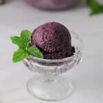 dessert glass holding a scoop of blueberry mint nice cream, garnished with fresh mint.
