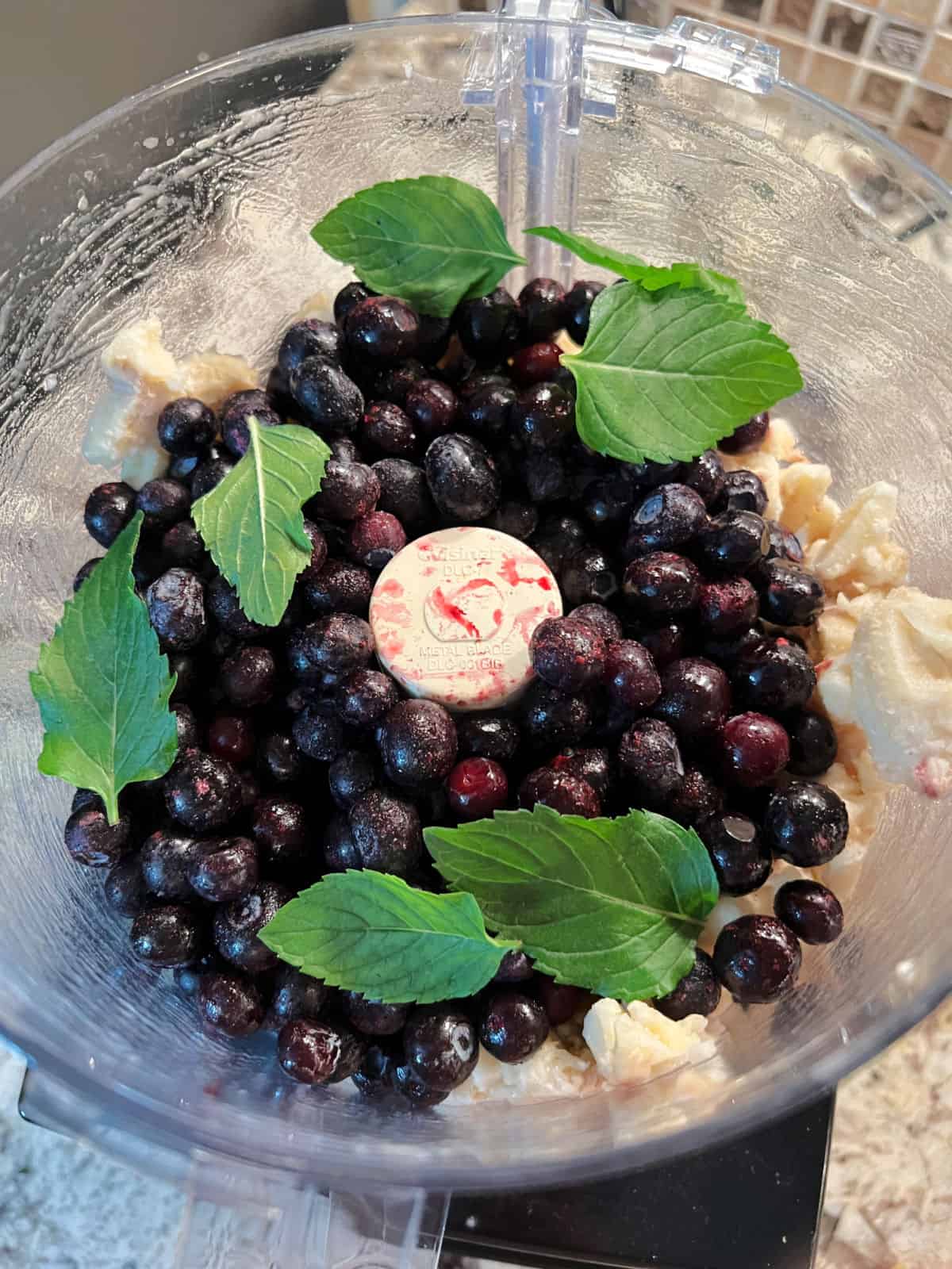 food processor with bananas, blueberries and mint leaves ready to be mixed.