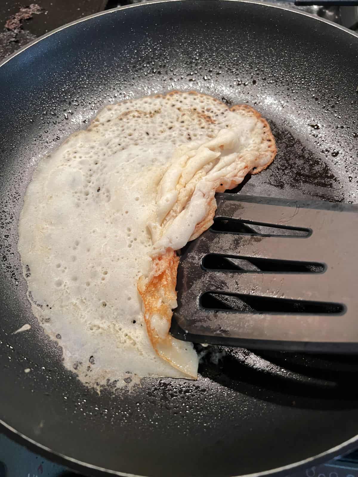 crepe in a skillet folding up as a spatula tries to get under it to flip.