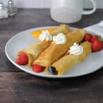 3 crepes made from pancake mix on a plate rolled with fruit and dolloped with whipped cream.