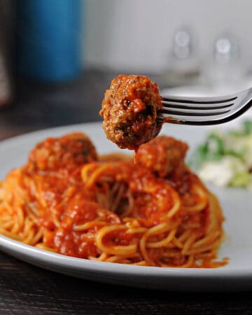 ricotta meatball on a fork above a plate of spaghetti.