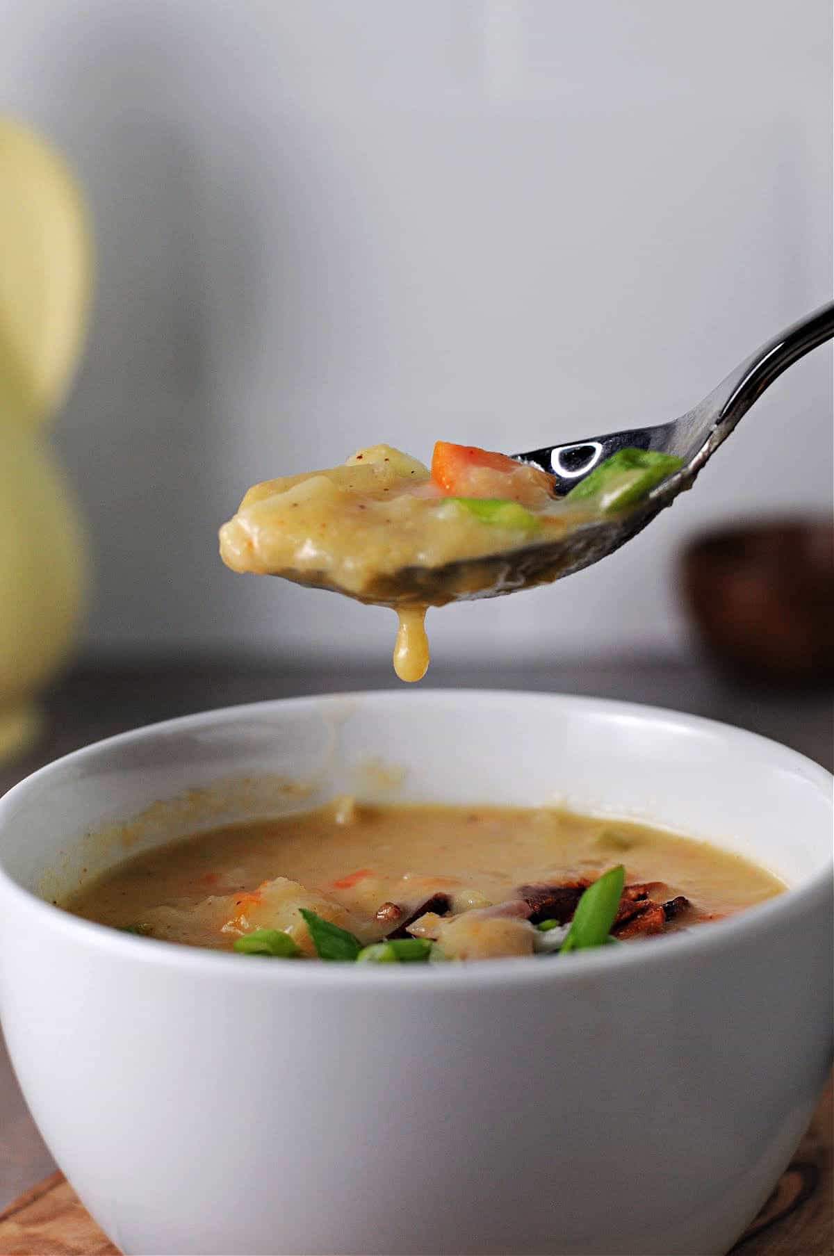 spoon of potato soup held above a bowl full of soup.