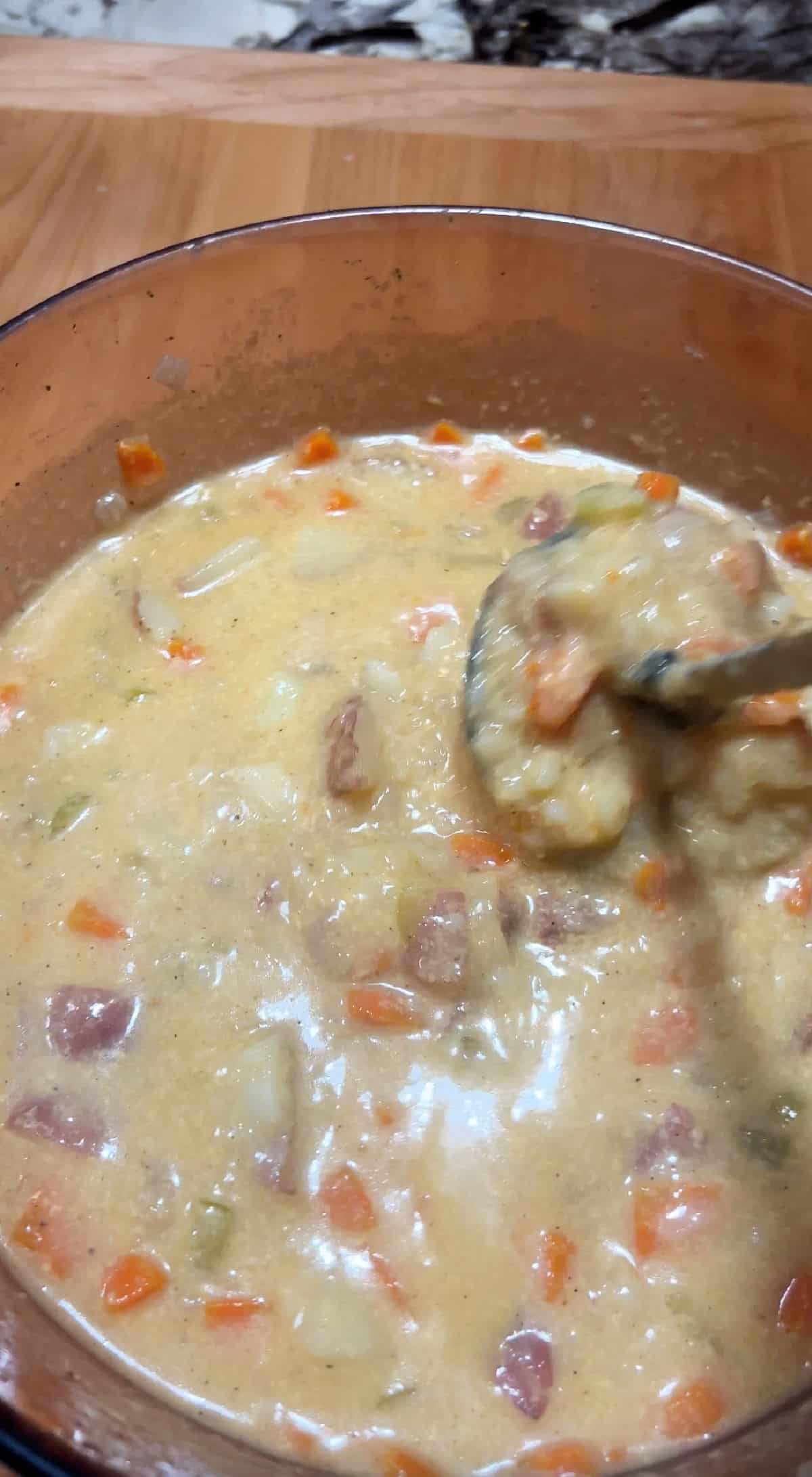 a potato masher is mashing the potatoes in the soup pot.