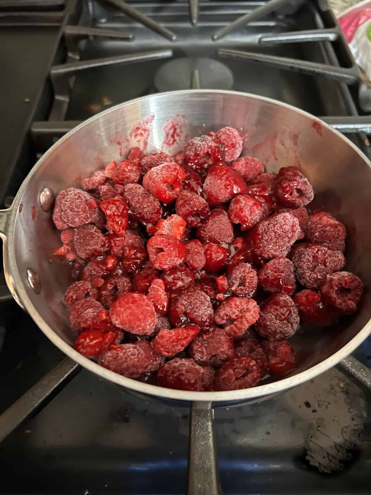 frozen raspberries with jam starting to cook in saucepan.