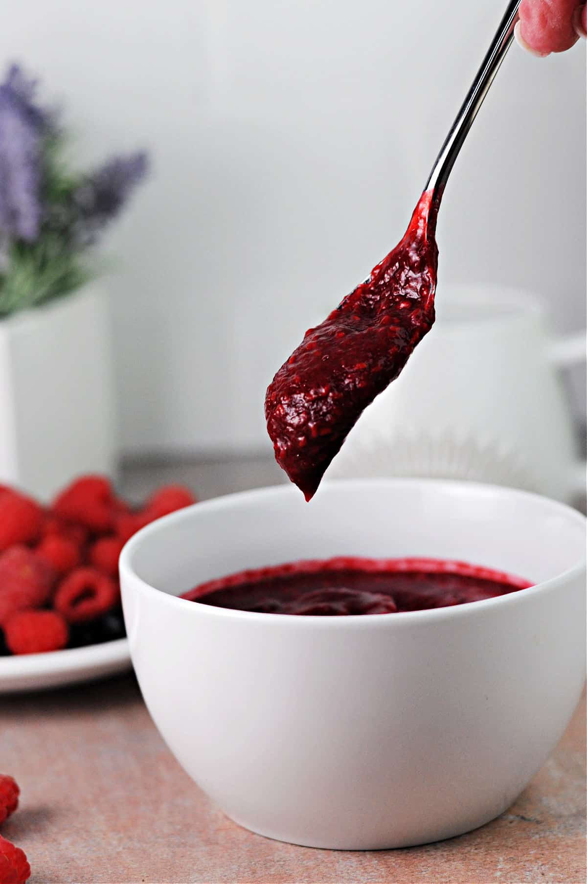 spoon drippping keto rasp berry sauce back into the bowl.