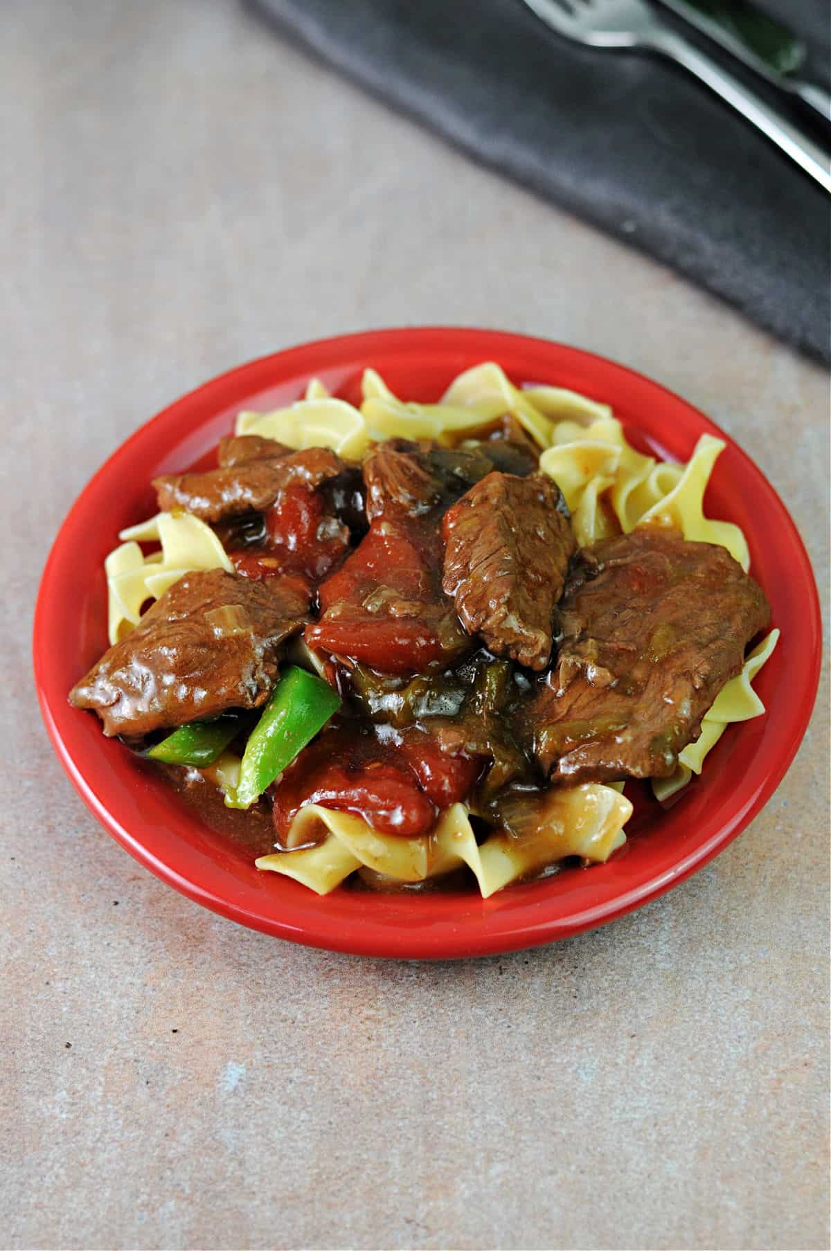pepper steak and noodles on a small red plate.