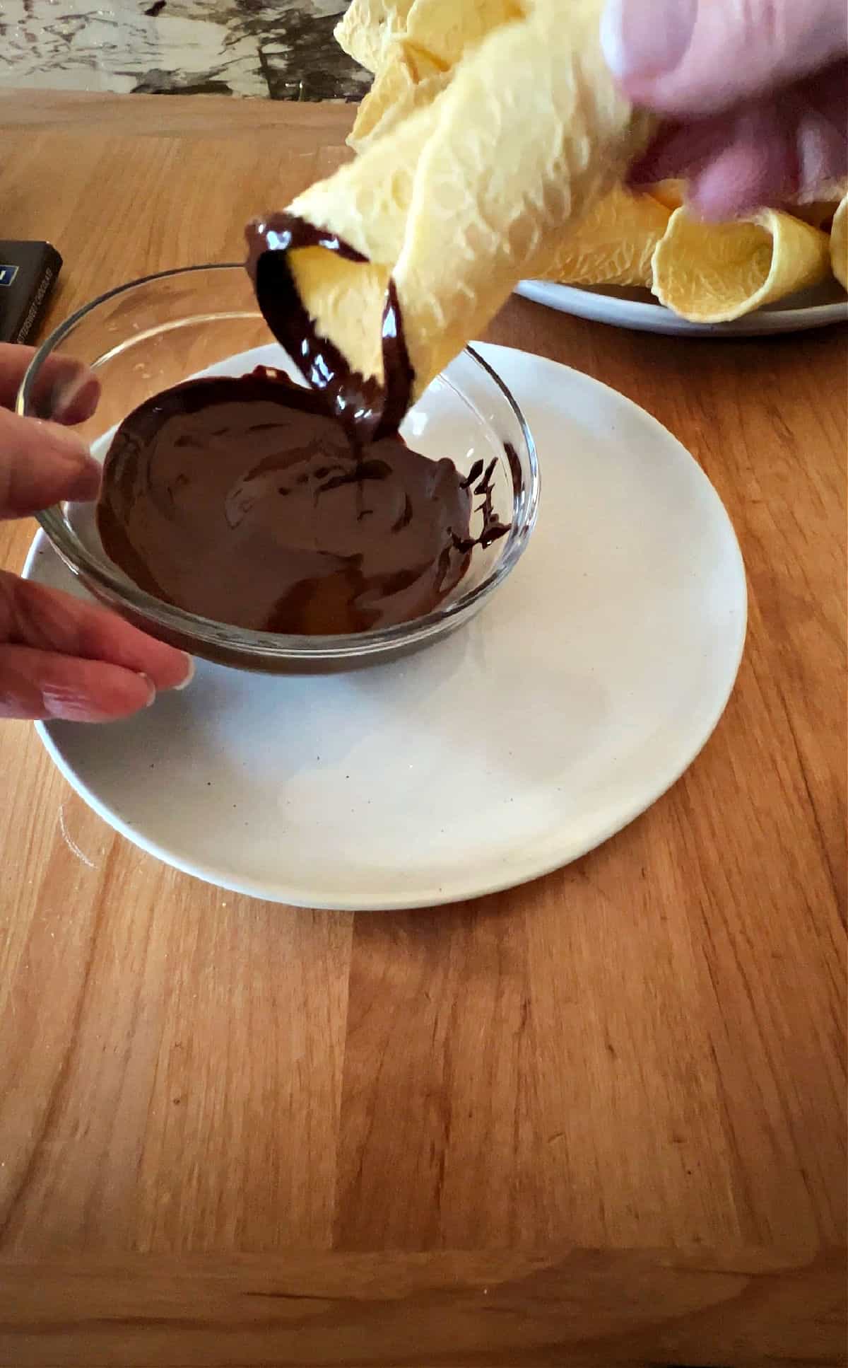 dipping a krumkake into melted chocolate.