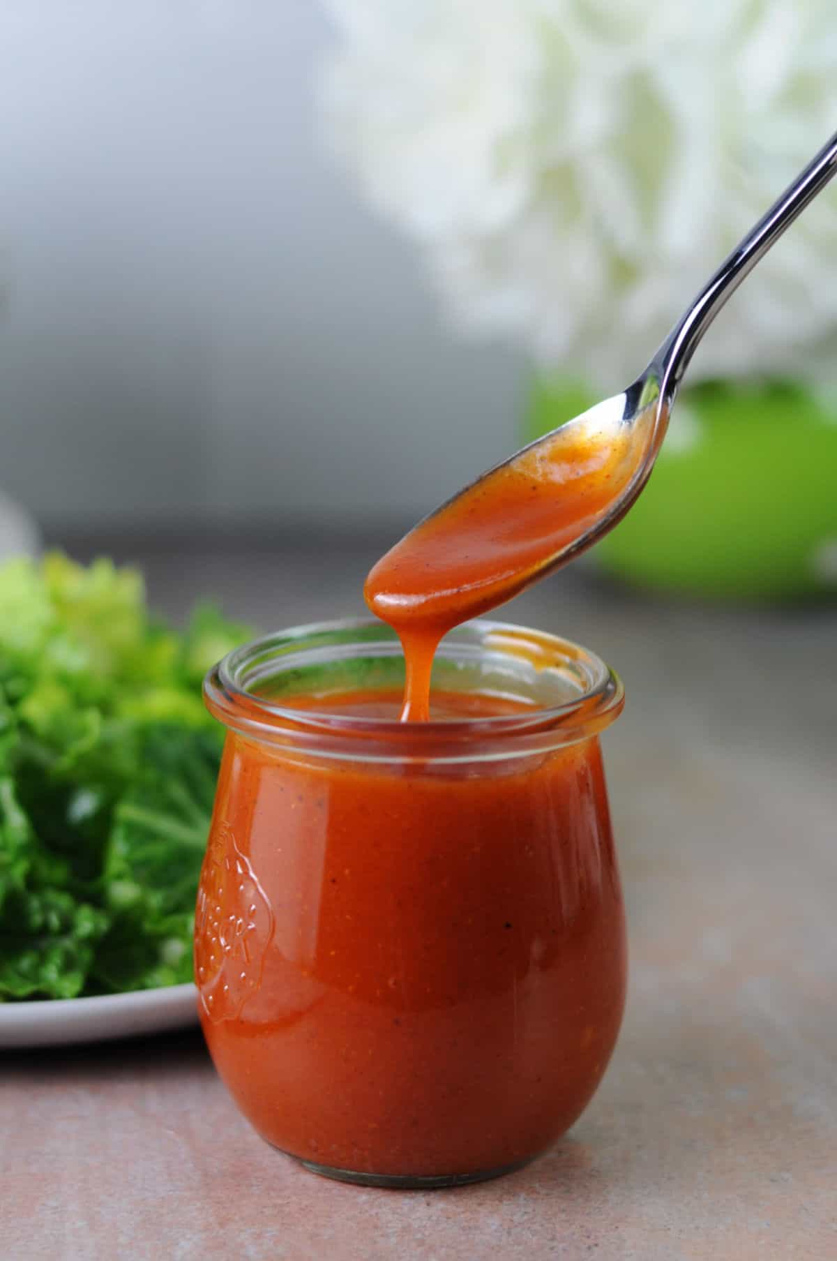 a spoon pouring salad dressing into a small jar.